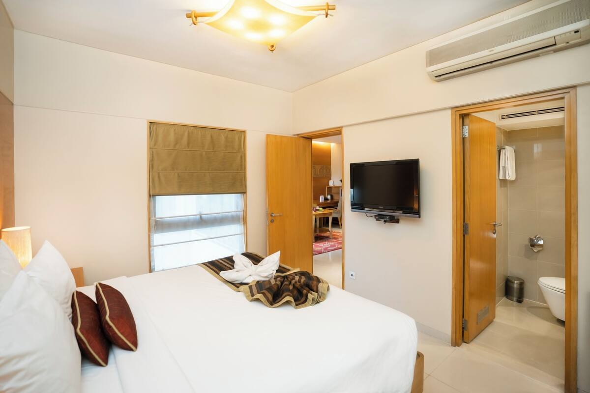 A hotel room with a bed, a television, a shower, and a wardrobe.