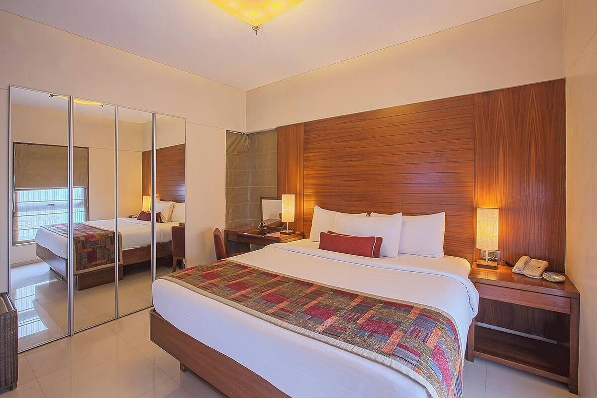 A hotel room with a large bed, a wooden headboard, a mirror, a bedside table with a lamp, and a telephone.