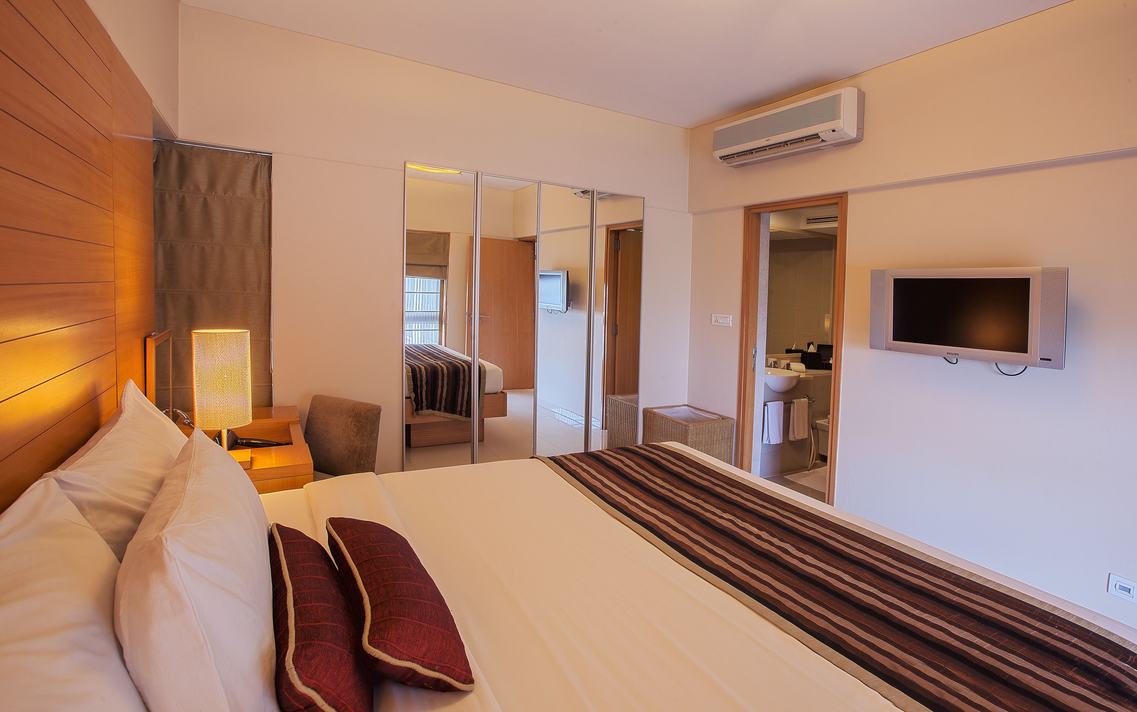 A hotel room with a bed, a TV, a bathroom, and a mirror.