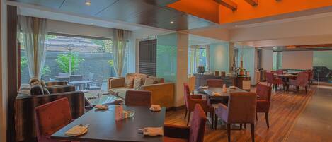 A modern dining area with wooden flooring, cushioned seating, and large windows offering a view of the outdoors.