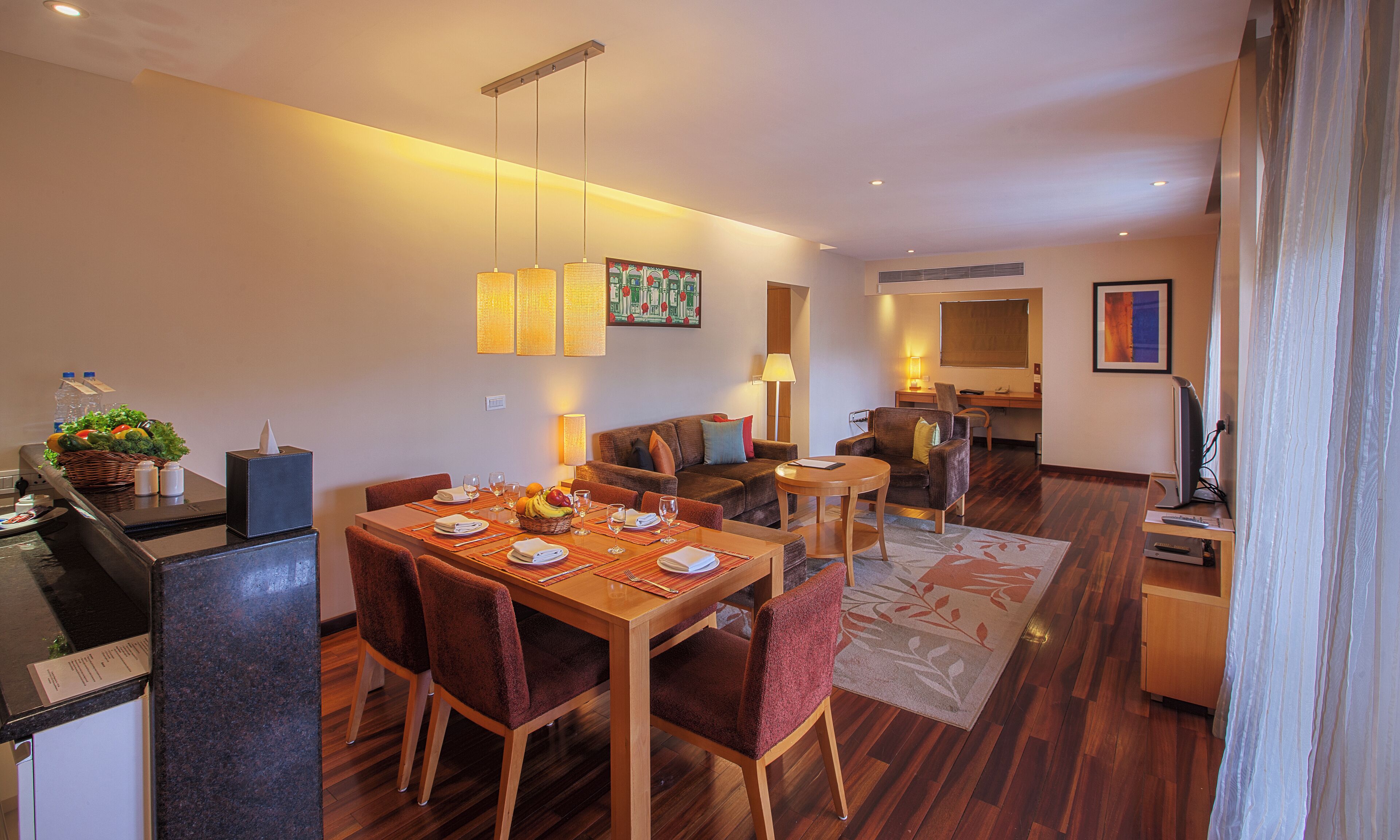 A modern hotel room with a dining area, a living area, and a kitchenette.