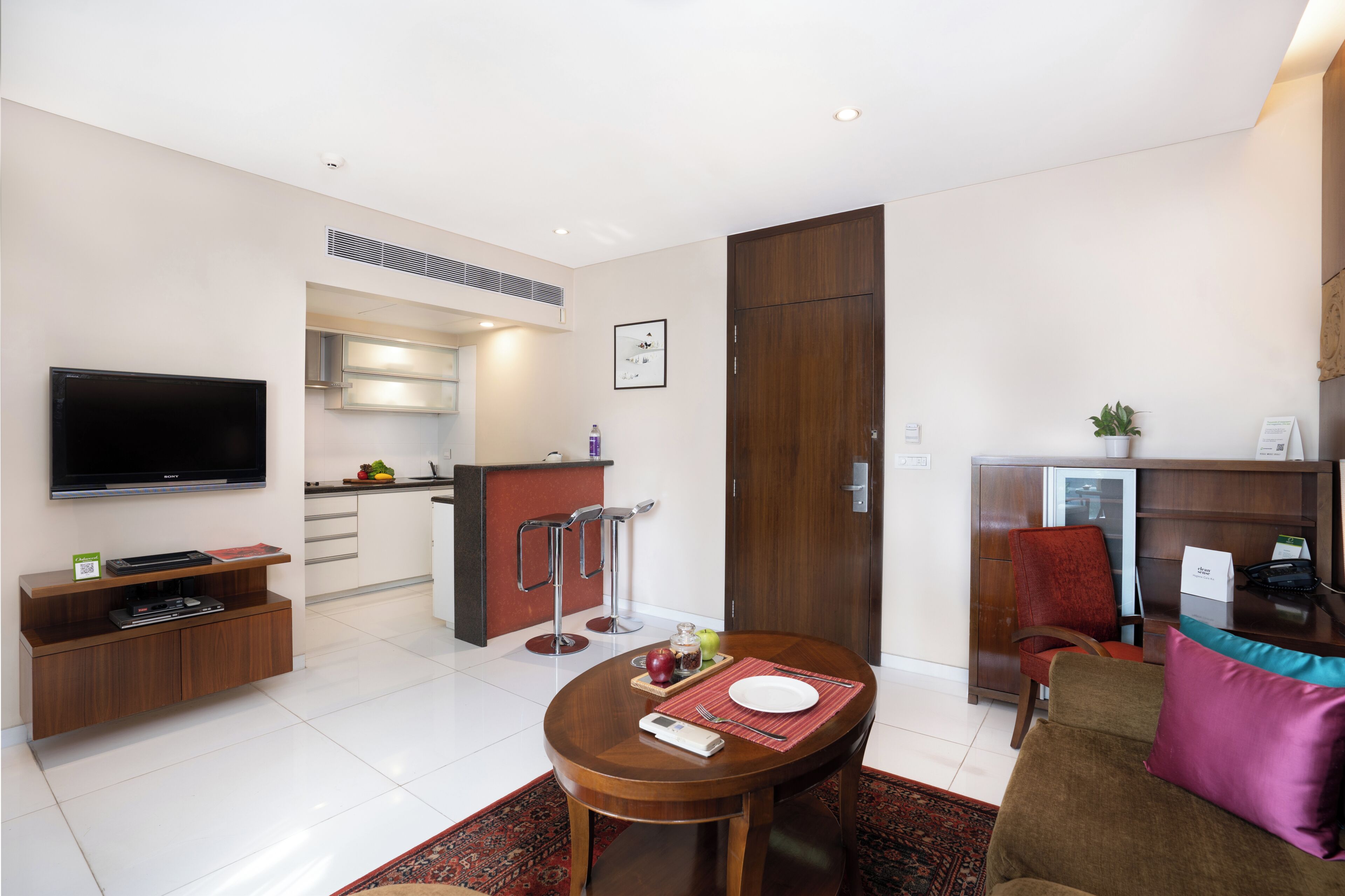 A modern hotel room with a dining area, kitchenette, and a TV mounted on the wall.