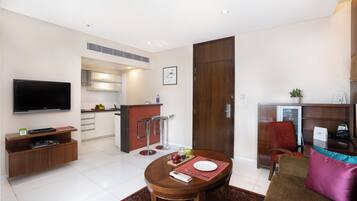 A modern hotel room with a dining area, kitchenette, and a TV mounted on the wall.