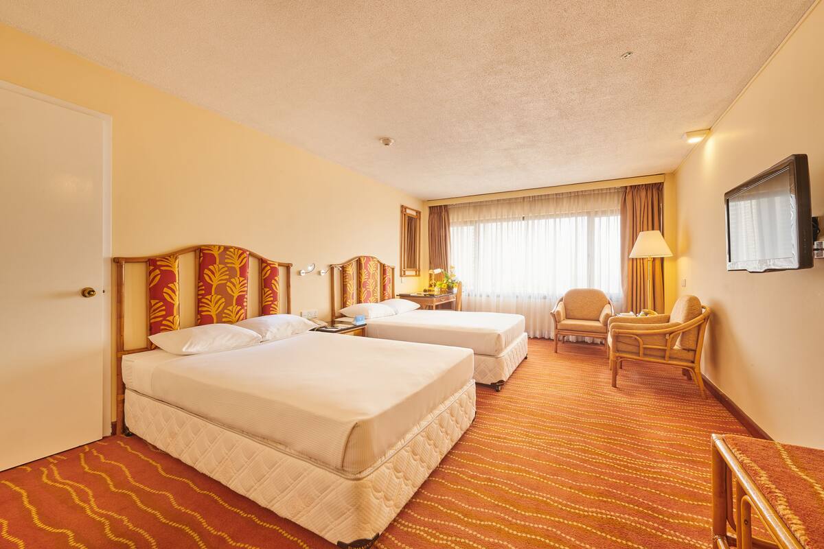A hotel room with two beds, a desk, a chair, a television, and a window with curtains.