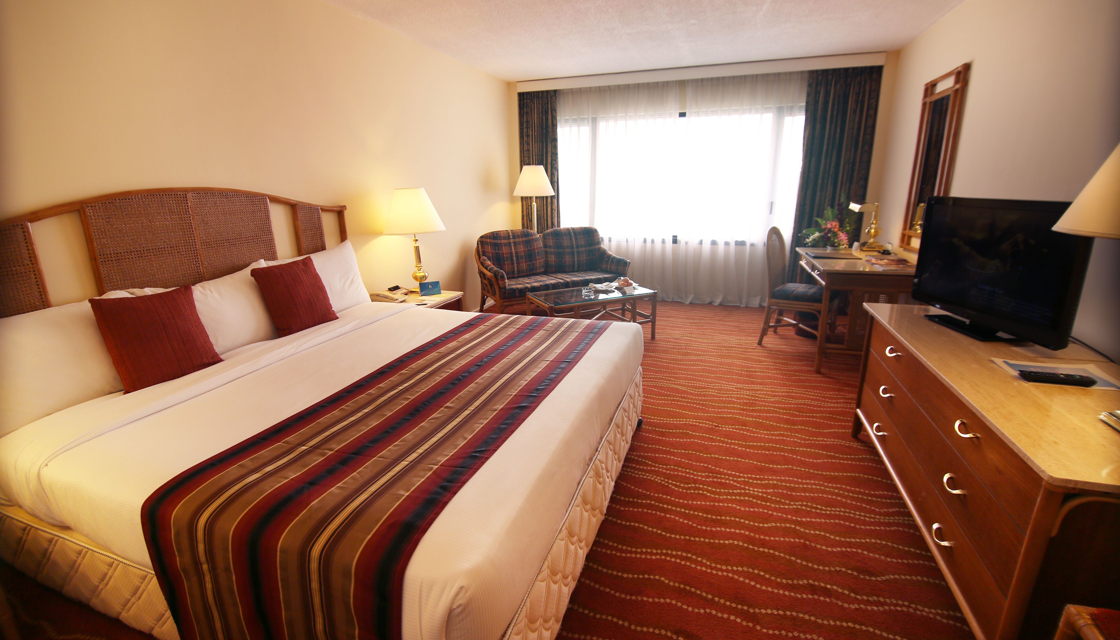 A hotel room with a large bed, a desk with a television, a chair, and a lamp.