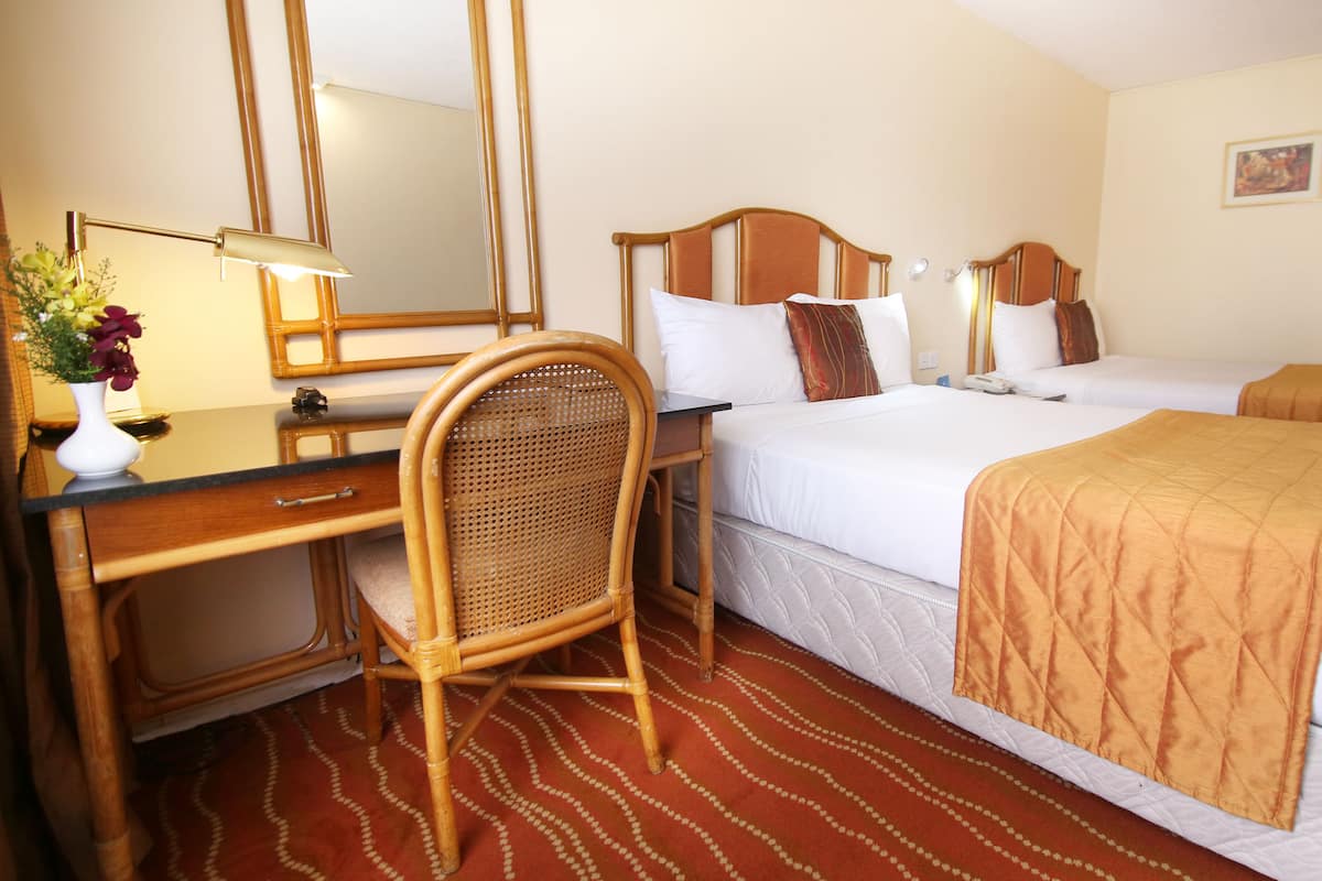 A hotel room with a bed, a desk with a lamp, a chair, and a mirror.