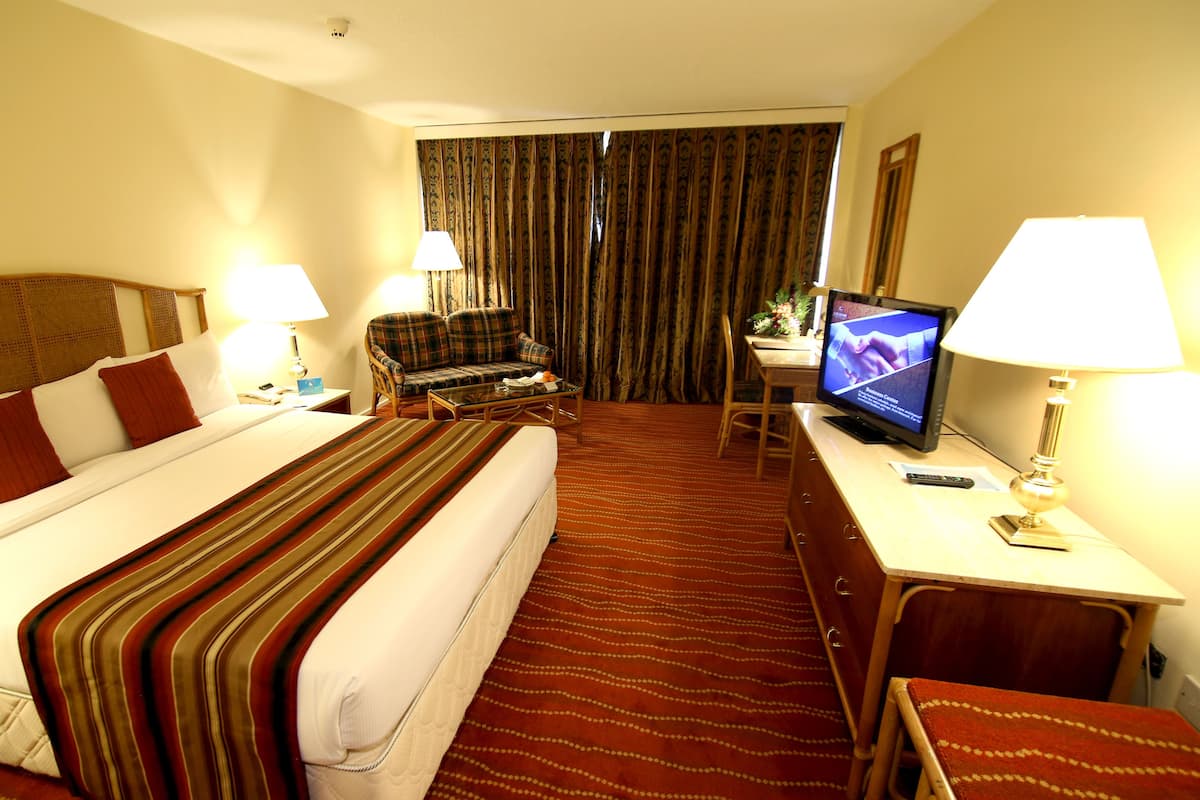 A hotel room with a large bed, a sofa, a desk with a computer, and a TV.