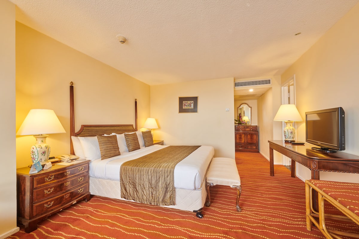 A hotel room with a bed, bedside tables, a TV, and a mirror.