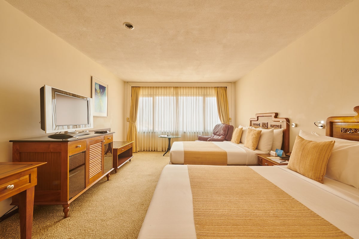 A hotel room with a large bed, a desk with a television, a small table, and a window with curtains.