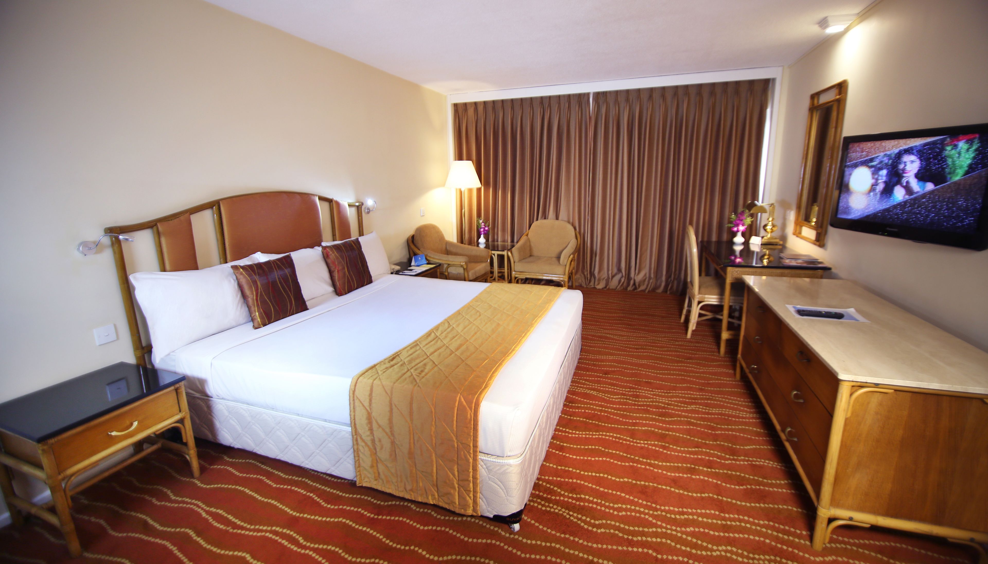 A hotel room with a large bed, a desk, a chair, a television, and a window with curtains.