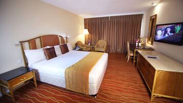 A hotel room with a large bed, a desk, a chair, a television, and a window with curtains.