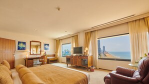 A hotel room with a large bed, a desk, a television, and a view of the beach. - Galadari Hotel (Colombo)