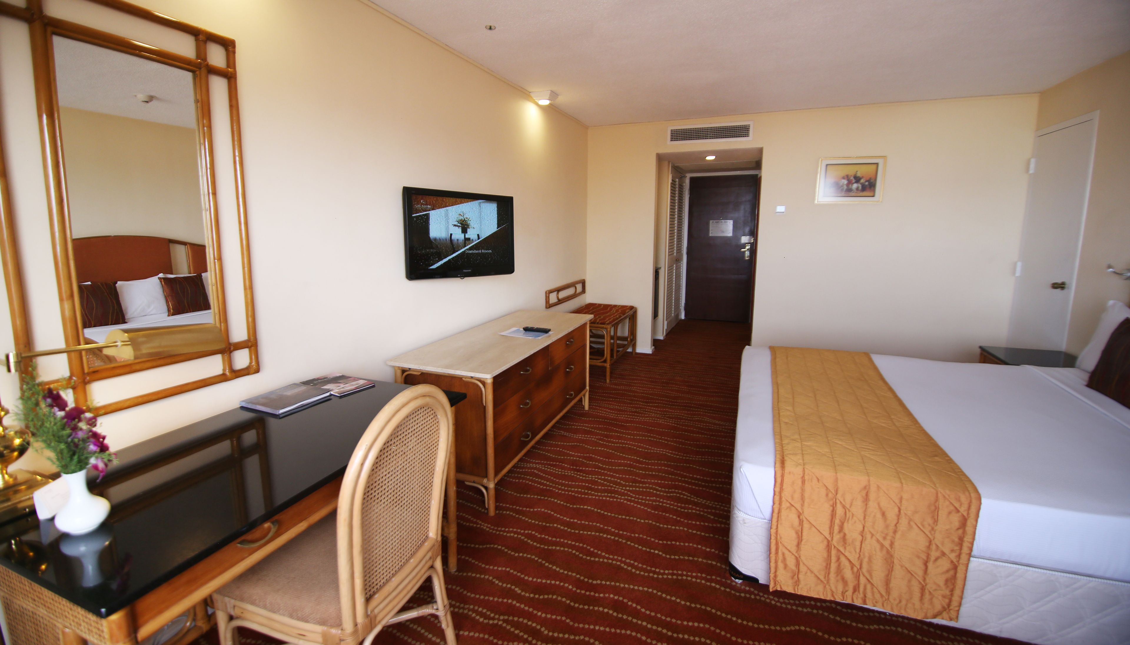 Een hotelkamer met een bed, een bureau, een stoel, een spiegel, een televisie en een deur naar een andere kamer.