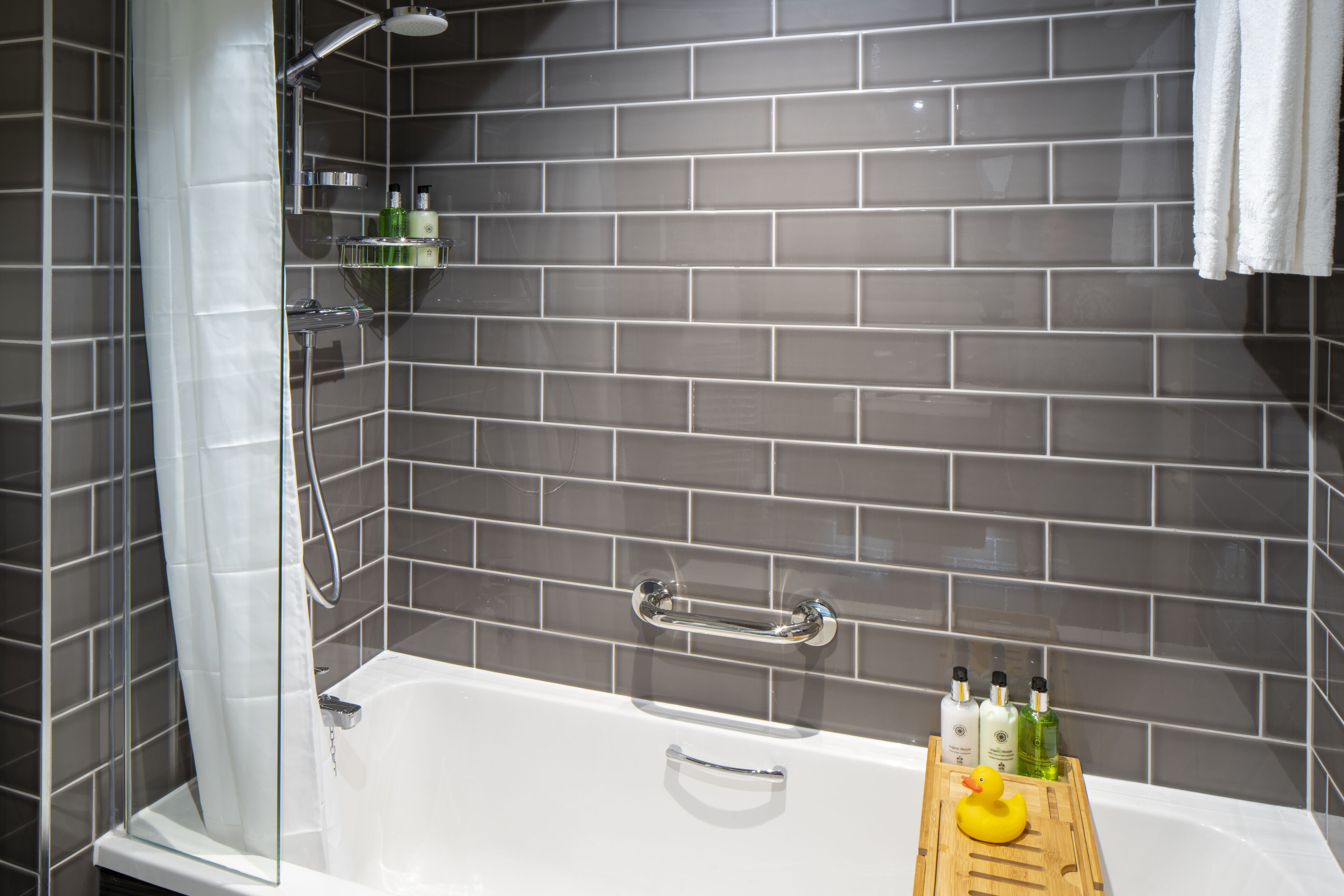 A modern bathroom with a bathtub, shower, and a wooden tray with toiletries.