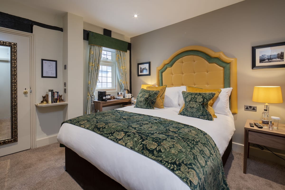 Een hotelkamer met een groot bed, een nachtkastje met een lamp, een spiegel en een raam met gordijnen.