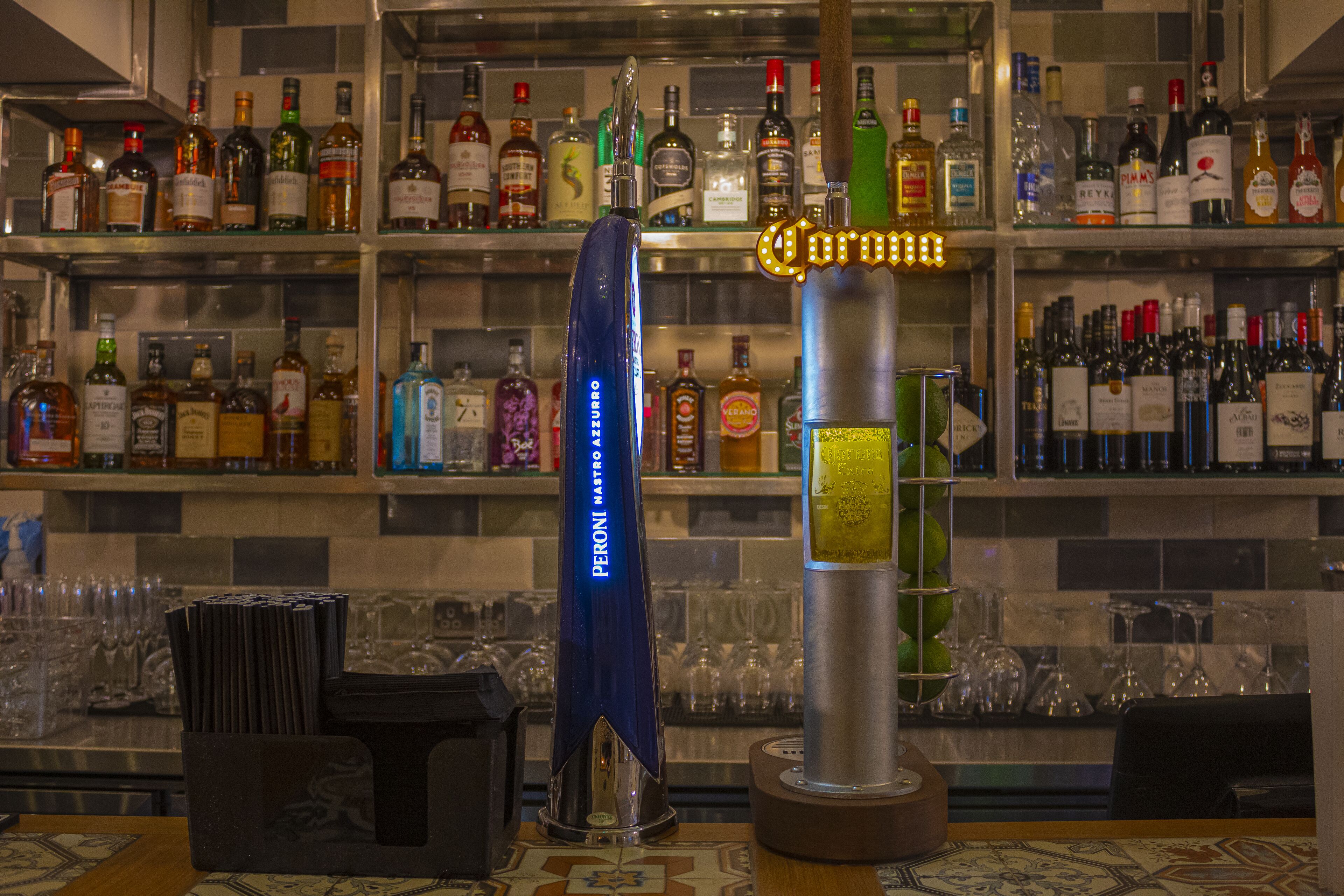 A bar area with shelves of liquor bottles, a blue bar tool, and a Corona sign.