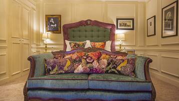 Una cama grande con un cabecero tapizado en verde y varios almohadones de colores, flanqueada por dos mesitas de noche con lámparas.