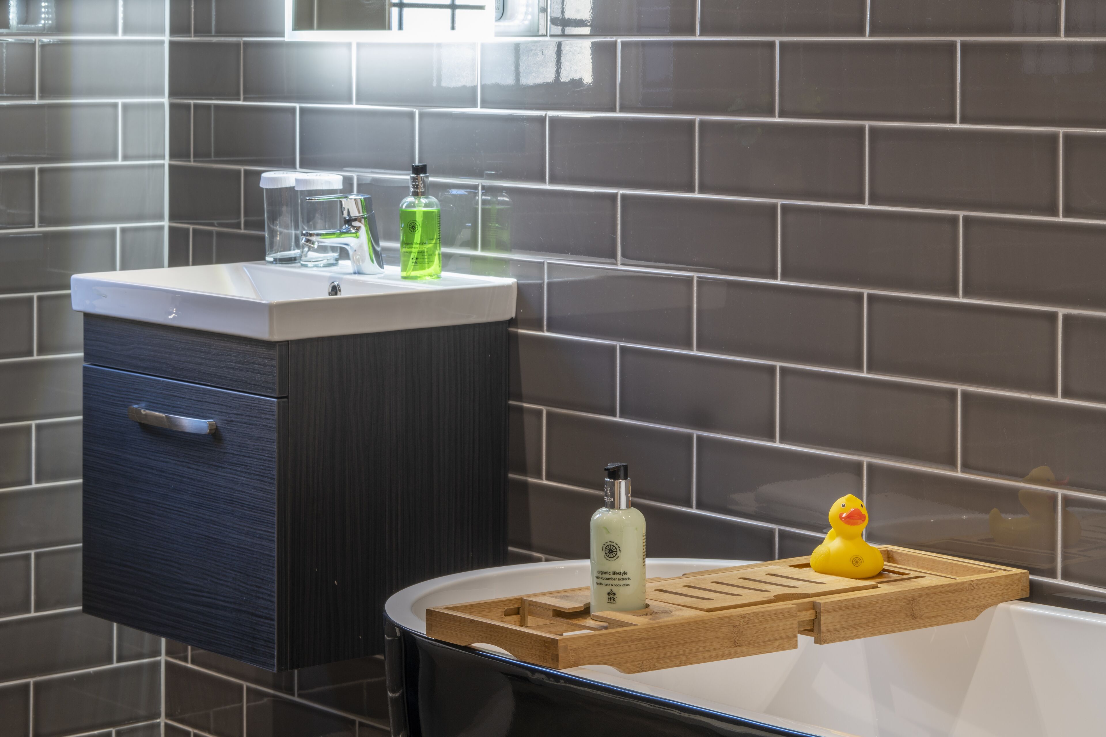 A bathroom with a modern design, featuring a dark cabinet, a white sink, and a wooden tray with a rubber duck.