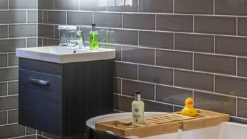 A bathroom with a modern design, featuring a dark cabinet, a white sink, and a wooden tray with a rubber duck.