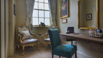 Una habitación con dos sillones decorados, un escritorio con ordenador y un espejo grande.