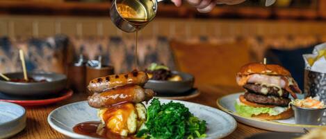 A dining table with various dishes including sausages, a burger, and a salad.