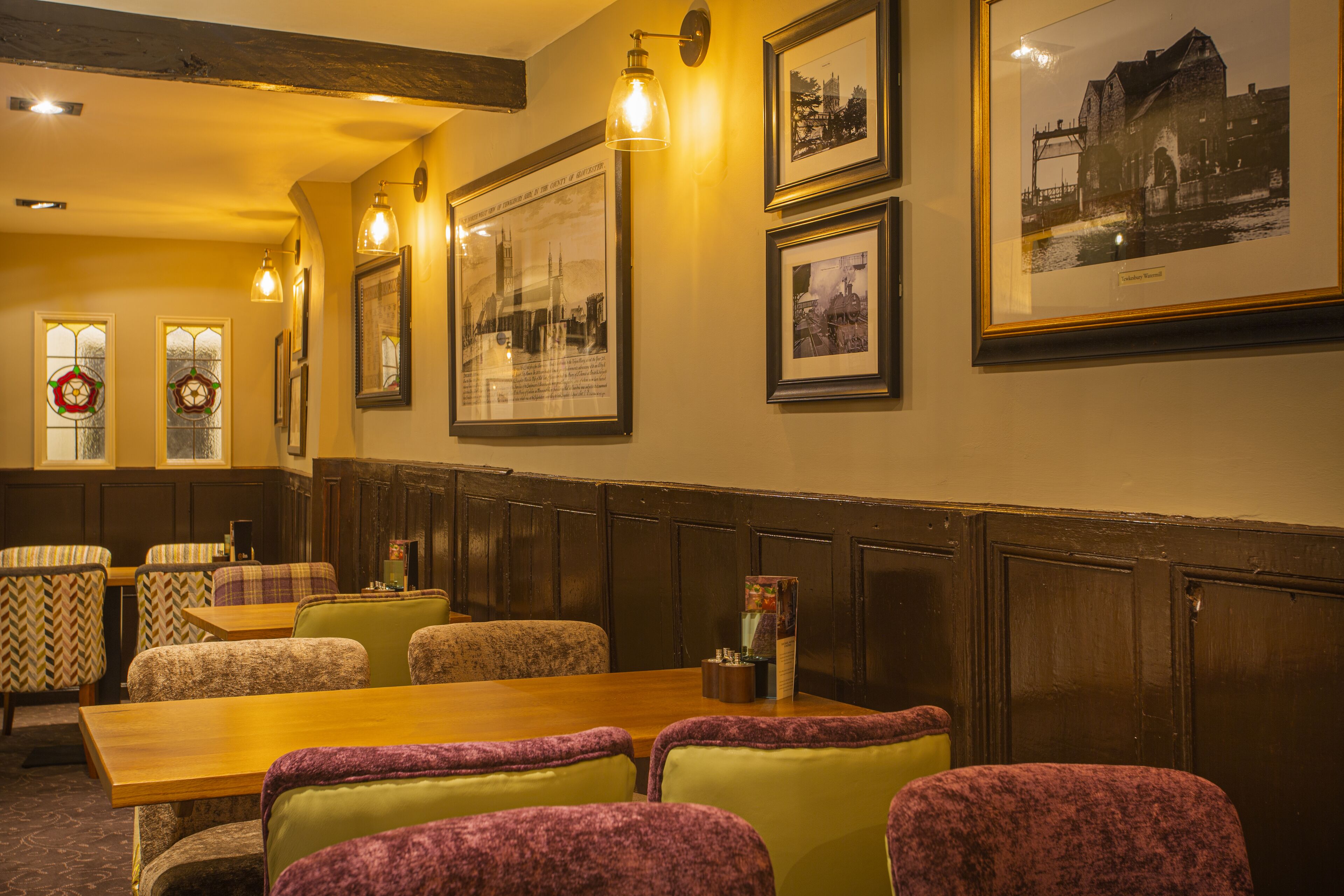 A restaurant with wooden tables and cushioned chairs, framed pictures on the wall, and a chandelier.