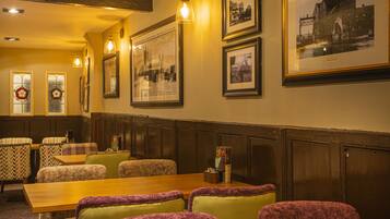 A restaurant with wooden tables and cushioned chairs, framed pictures on the wall, and a chandelier.