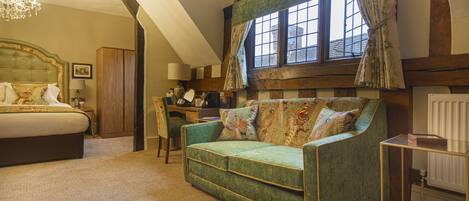 A bedroom with a large bed, a green sofa, a desk, and a window with curtains.