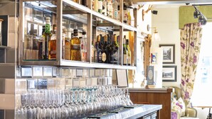 Een bar met flessen drank en een rij lege wijnglazen.