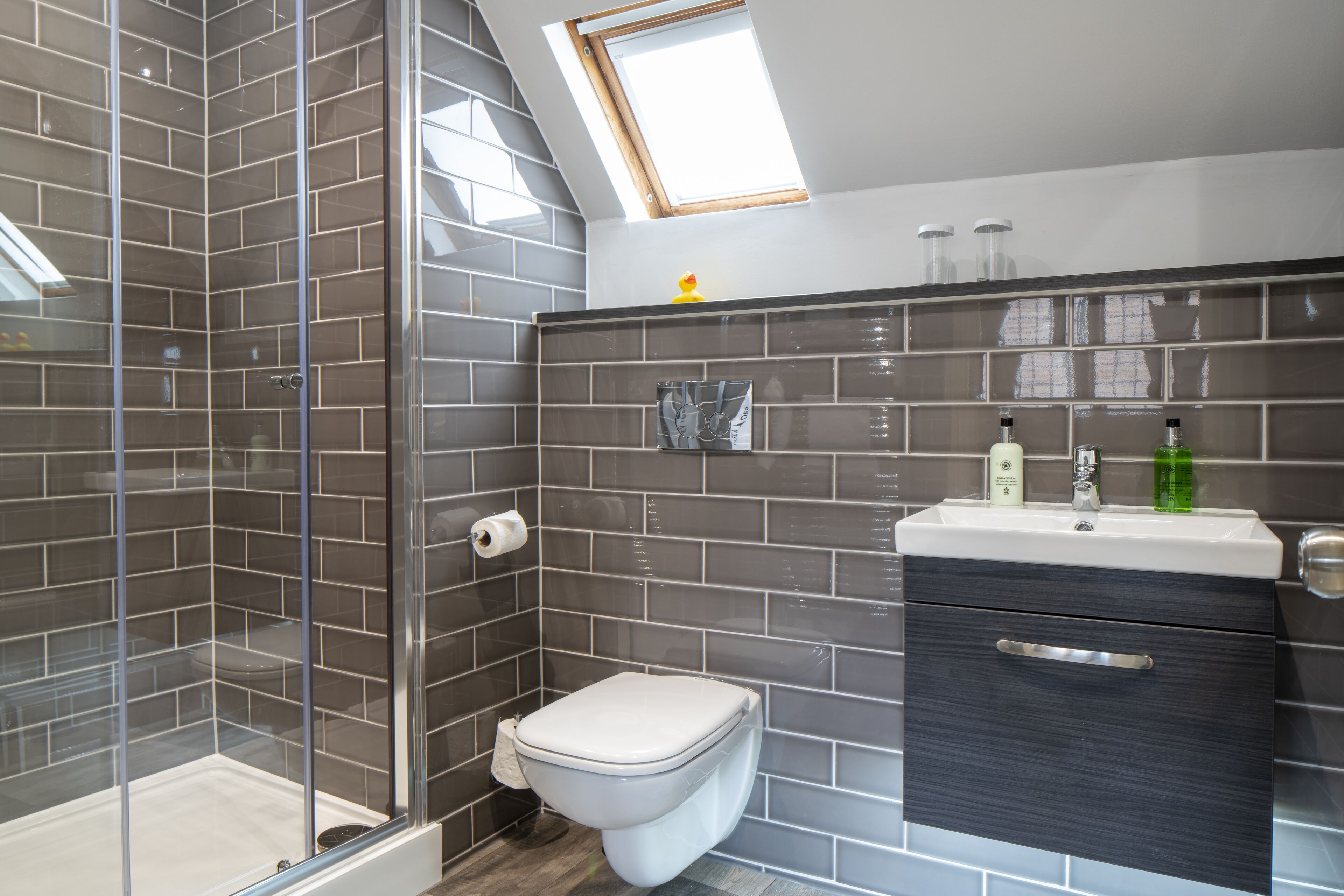 Une salle de bain moderne avec une douche à parois de verre, des toilettes et un lavabo avec un meuble sombre.