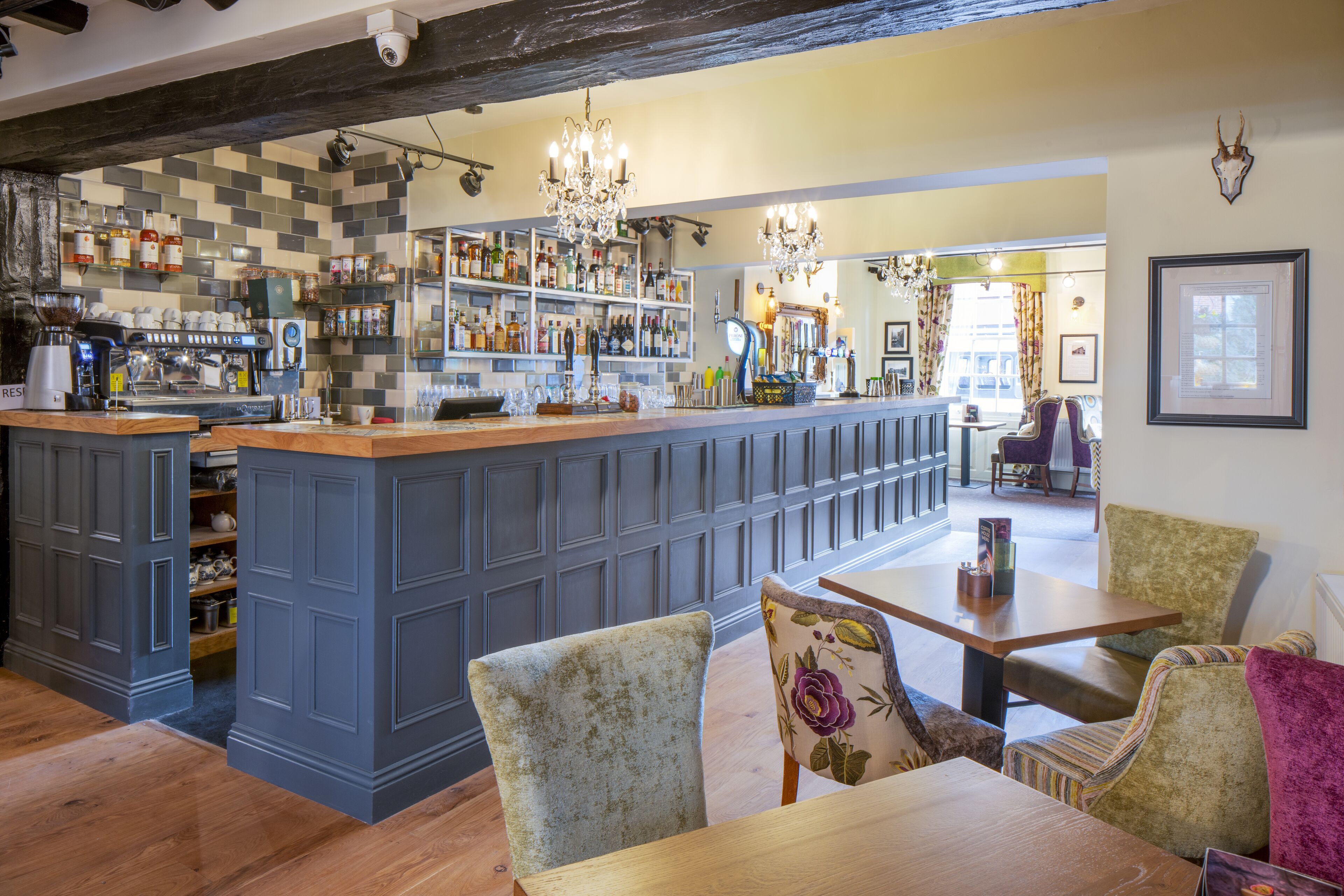 A bar area with a counter, shelves with bottles, and seating with floral cushions.