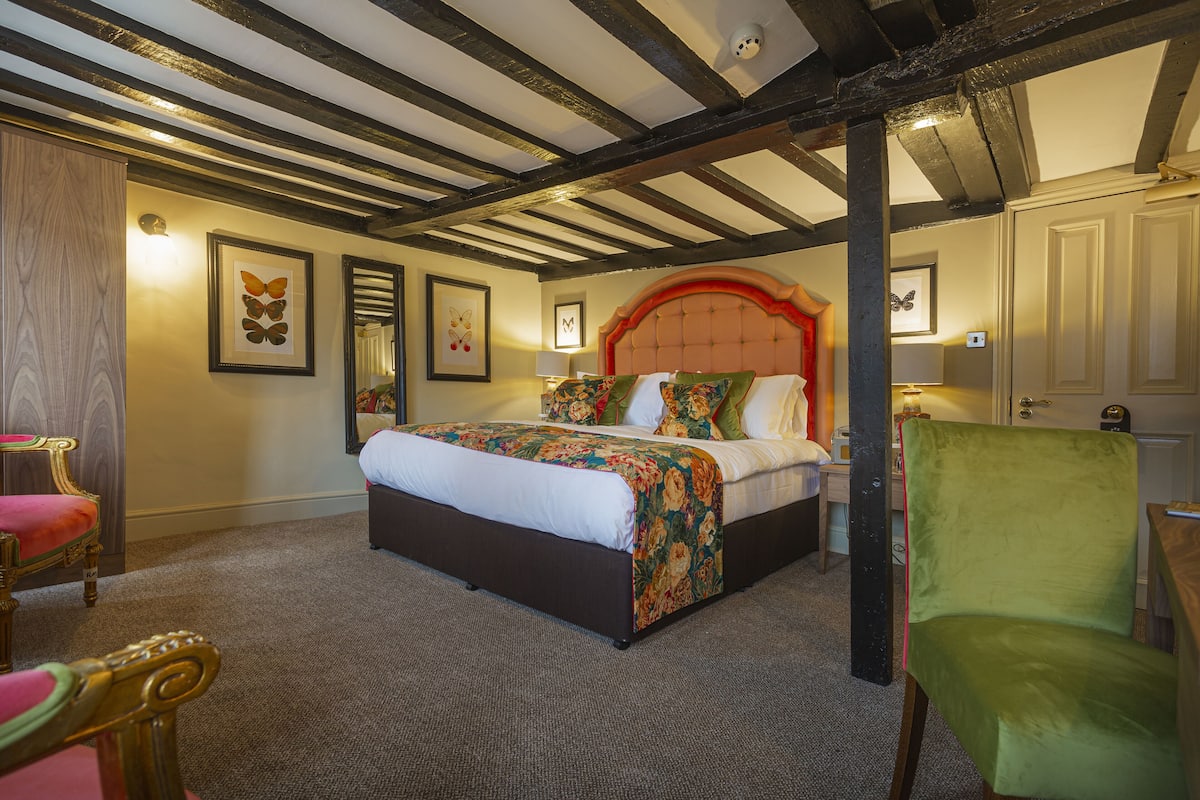Een slaapkamer met een groot bed, een houten stoel, een groene fauteuil en een houten kledingkast.