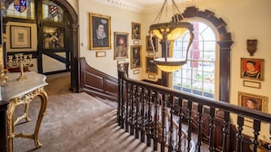 Een statige trap met sierlijke balustrades, een kroonluchter en omlijste portretten aan de muren.