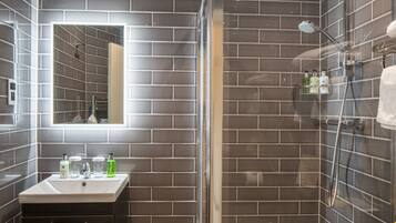 A modern bathroom with a glass-enclosed shower, a vanity with a mirror, and toiletries on the sink.