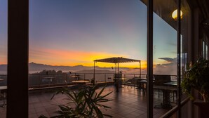 A terrace with tables and chairs, overlooking a sunset with mountains in the distance.