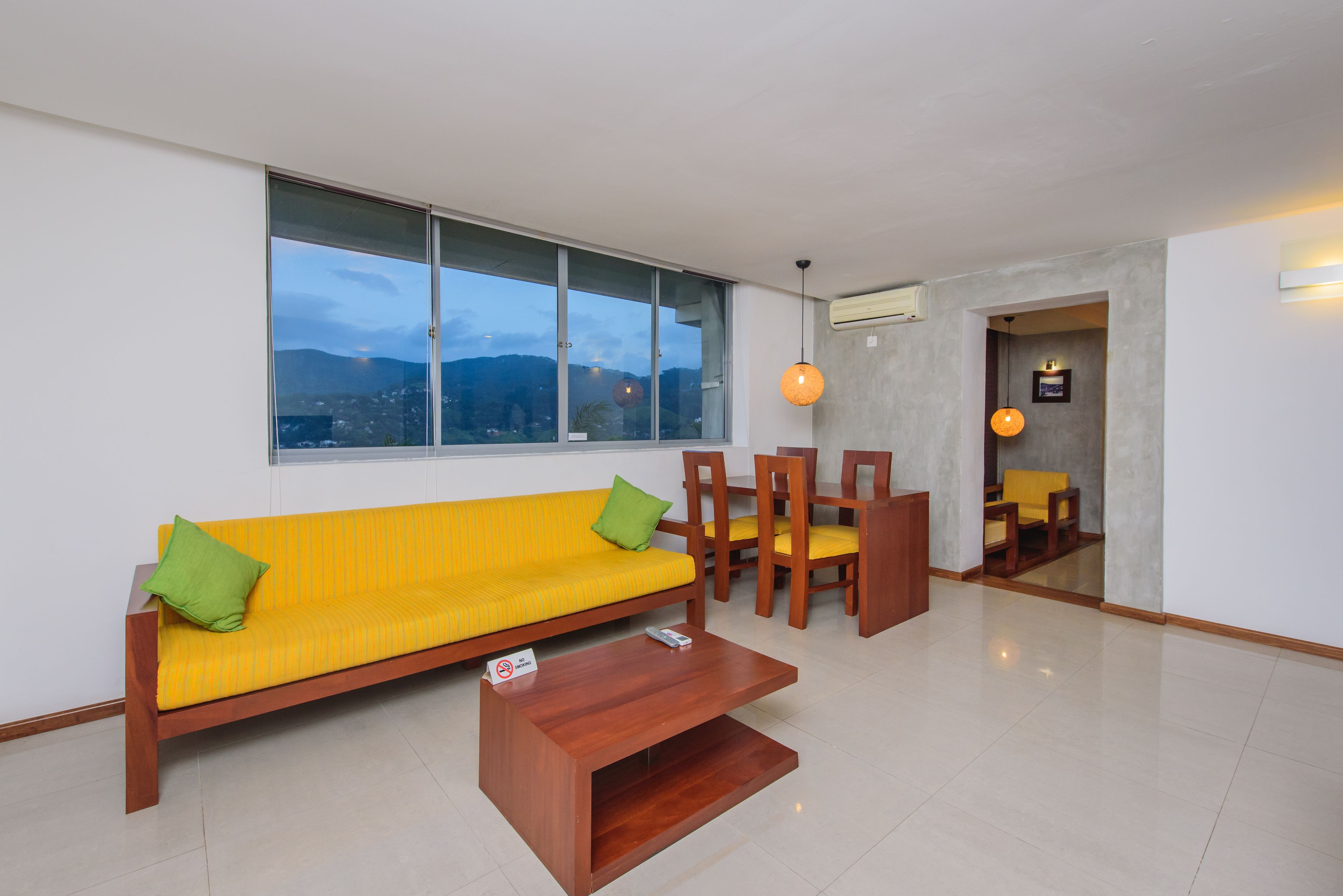 A modern living room with a yellow sofa, green cushions, wooden chairs, and a coffee table.