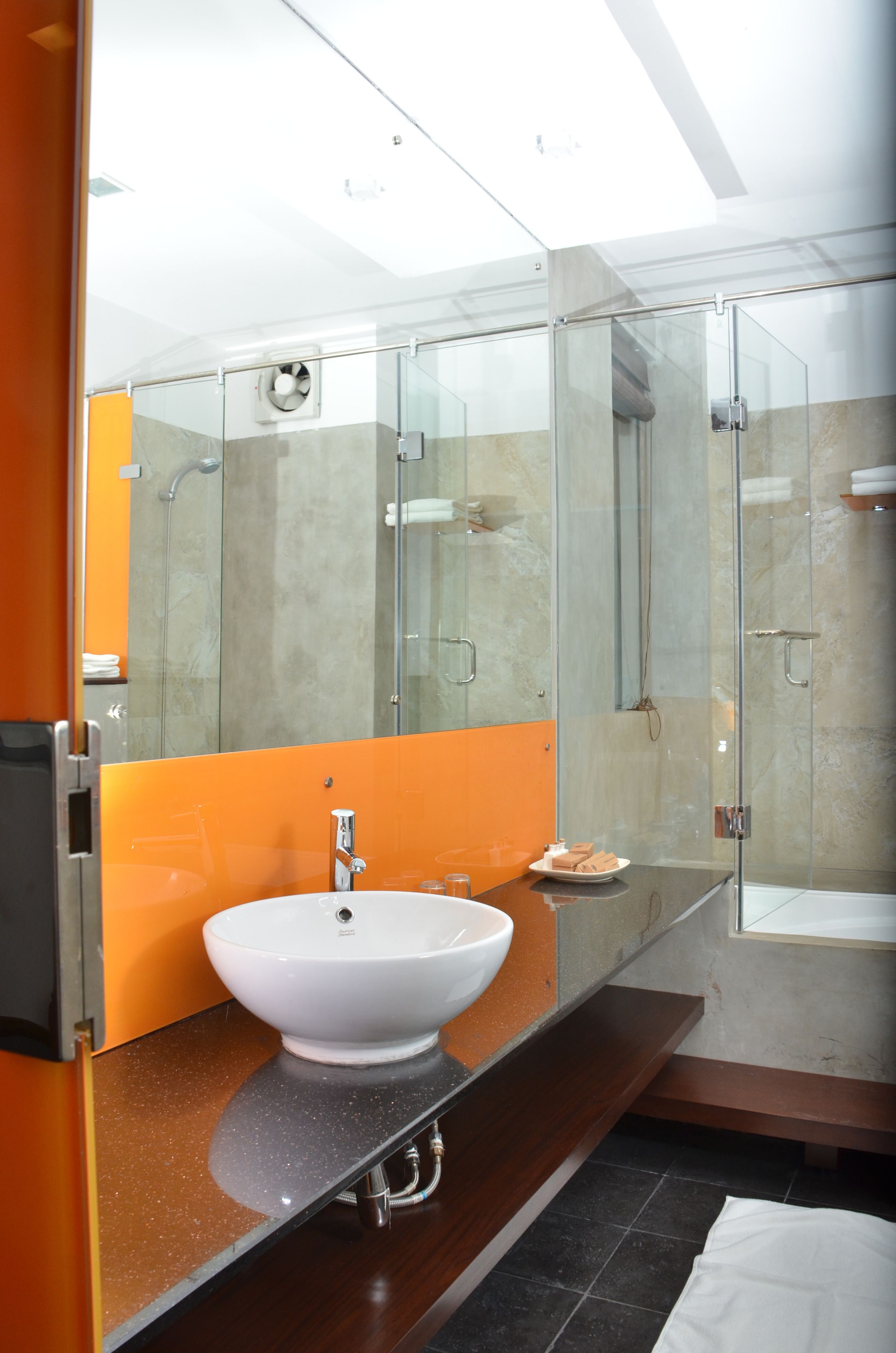 A modern bathroom with a glass-enclosed shower, a white sink, and an orange accent wall.