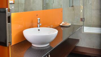 A modern bathroom with a glass-enclosed shower, a white sink, and an orange accent wall.