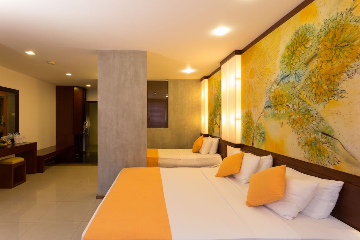 Habitación de hotel con dos camas, una zona de estar con un banco, un cuadro grande en la pared y vistas al pasillo.
