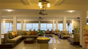 A spacious lobby with a large seating area, a central decorative bowl, ceiling fans, and large windows providing natural light.