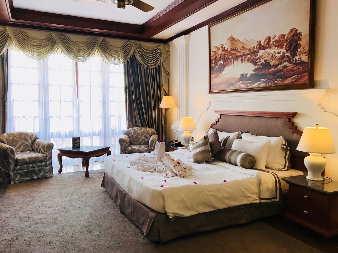 A hotel room with a large bed, two armchairs, a small table, and a painting on the wall.