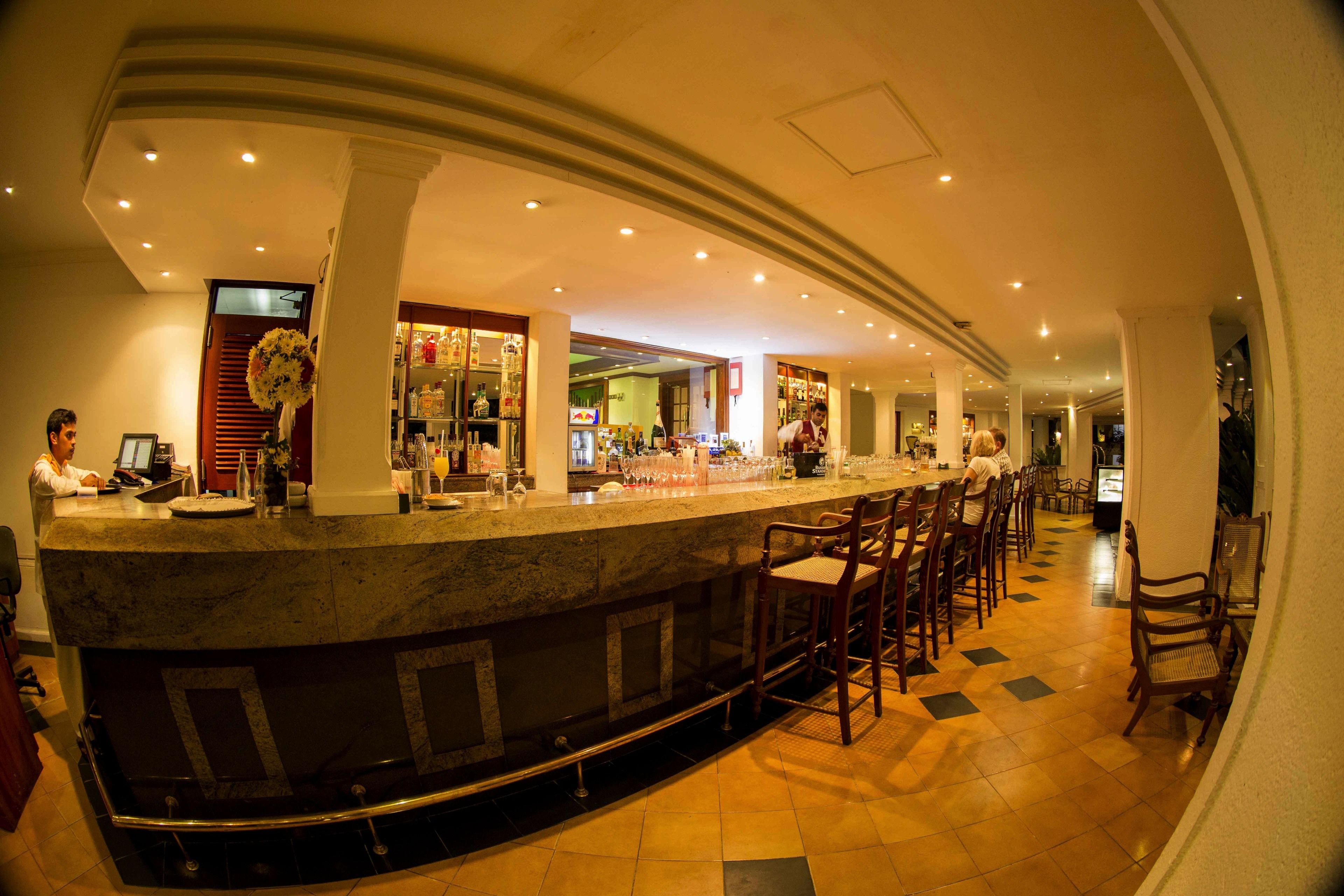 Zona de bar con mostrador curvo, varios taburetes y suelo de baldosas.