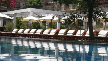 Un espace piscine agrémenté de chaises longues et de parasols, entouré d’arbres et d’immeubles.