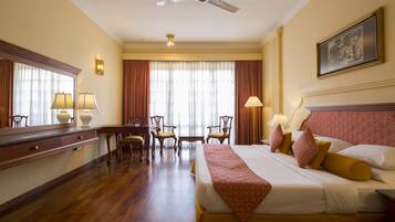 A hotel room with a large bed, a desk with a chair, a vanity with a mirror, and a ceiling fan.
