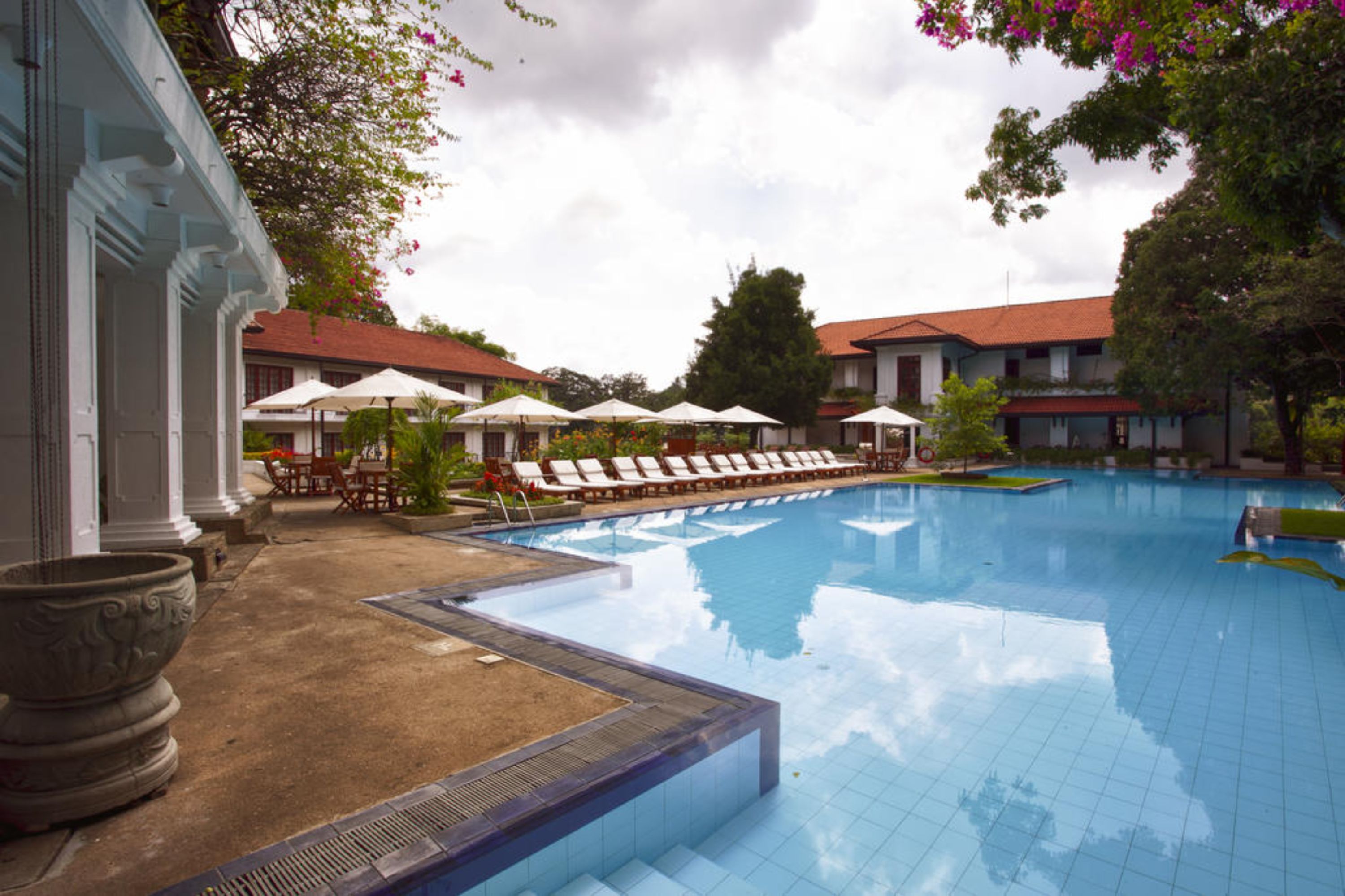 A swimming pool with lounge chairs and umbrellas, surrounded by buildings with red roofs.