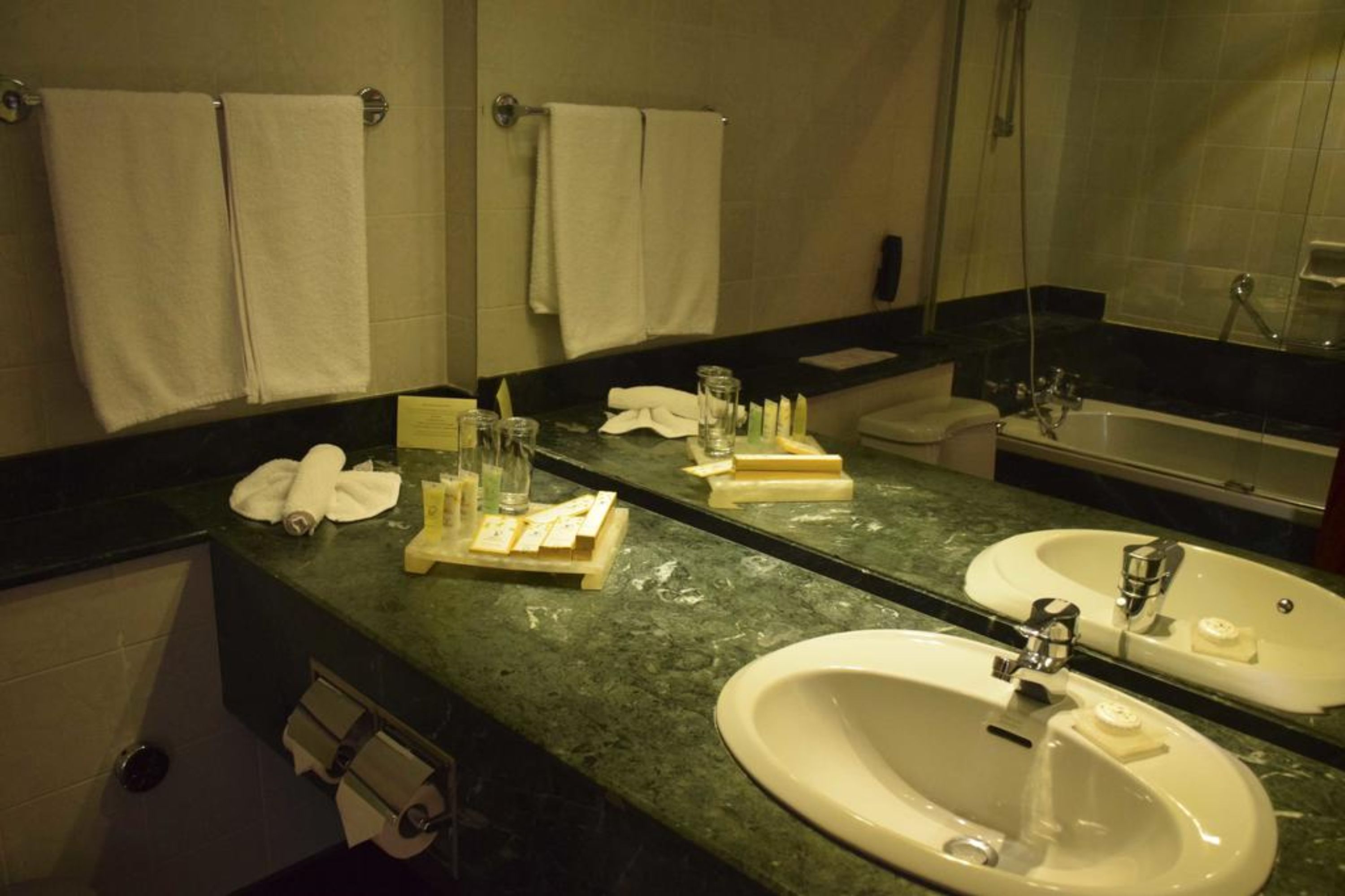 A bathroom with two sinks, a mirror, and towels hanging on the wall.