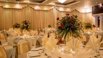 Un salón de banquetes con mesas redondas dispuestas para un evento formal, con manteles blancos, fajones dorados y centros de mesa florales.