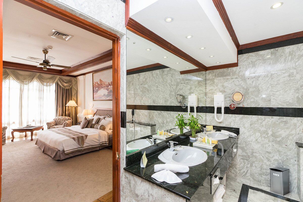 A hotel room with a large bed, a bathroom with a marble vanity, and a ceiling fan.
