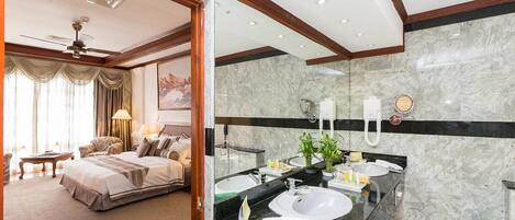 Habitación de hotel con una cama grande, un baño con tocador de mármol y un ventilador de techo.
