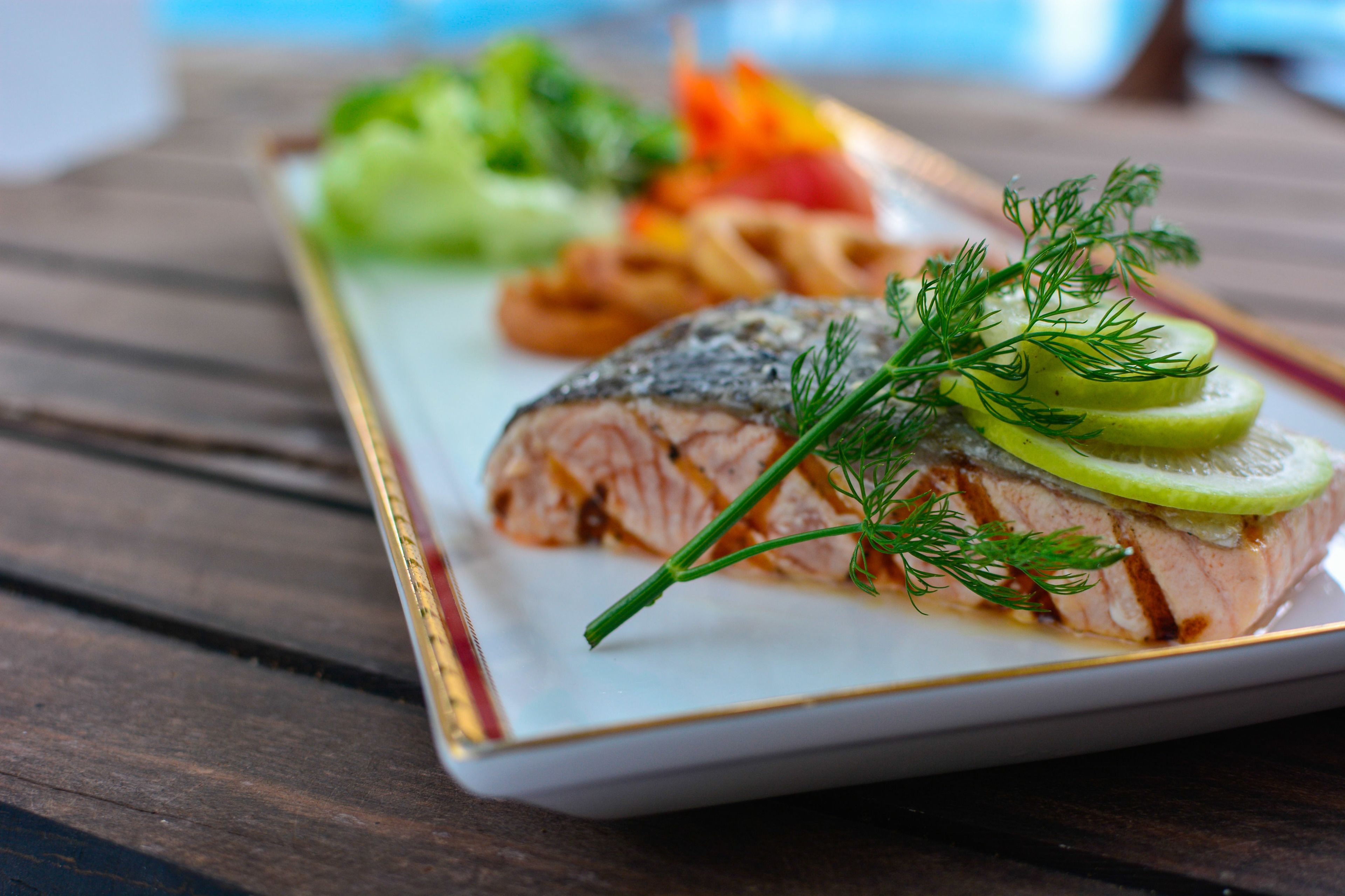 A plate of food with salmon, vegetables, and a garnish.